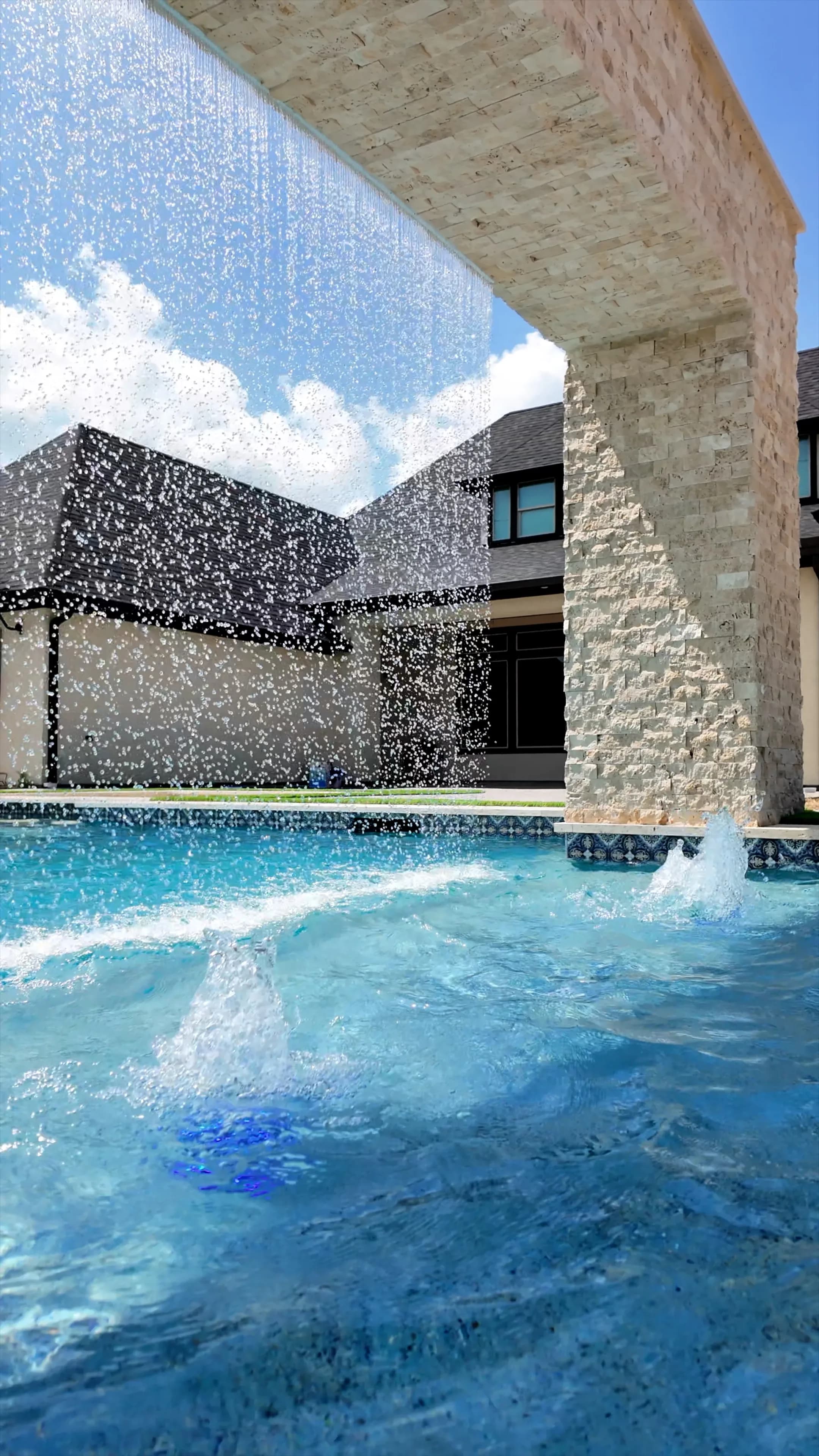 Rain-curtain water wall pouring from the travertine arch, with the home beyond