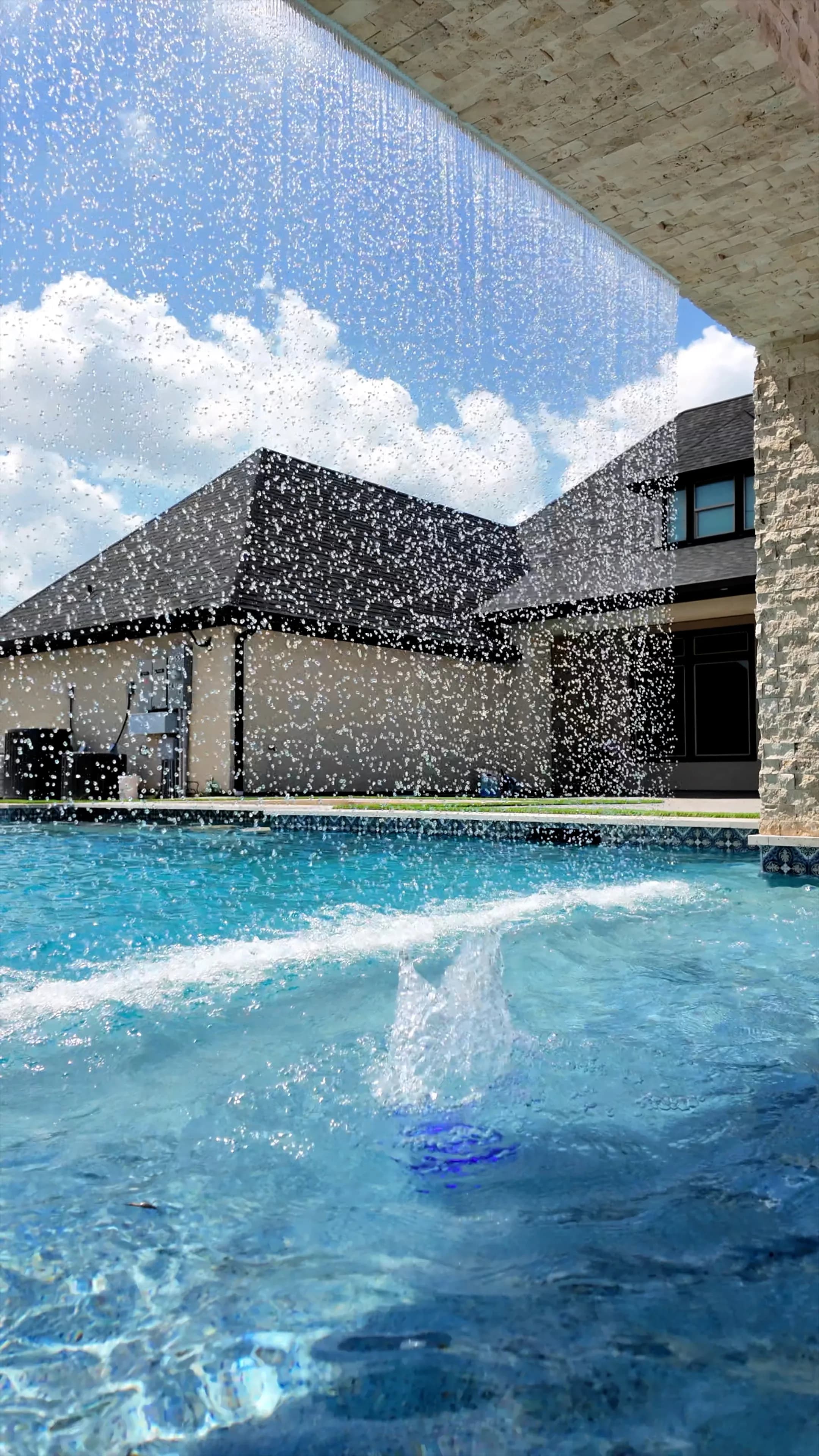 Sheets of falling water framing the house through the rain-curtain arch in Manvel, TX