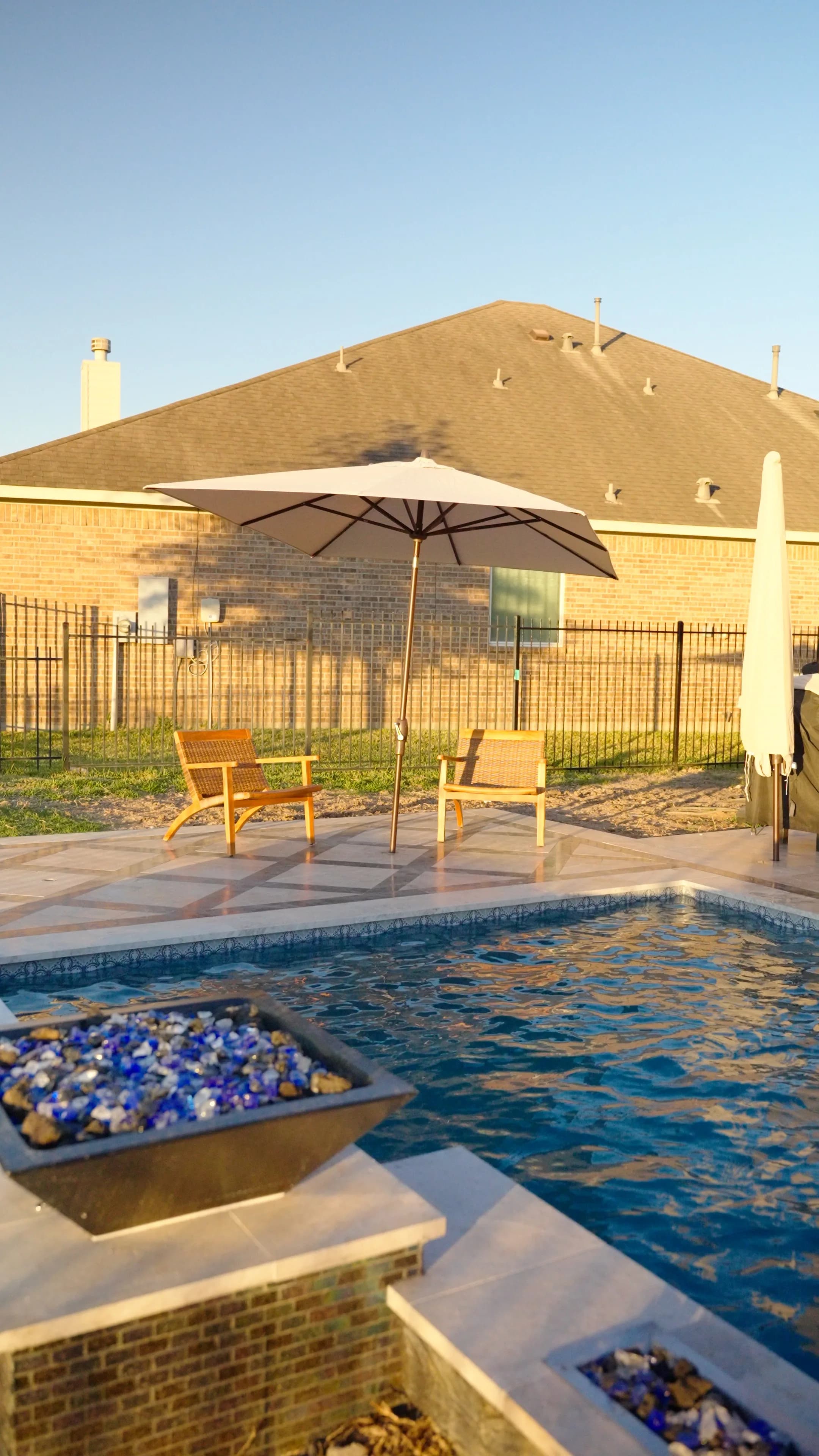 Fire bowl filled with blue glass beside the pool, with an umbrella and lounge chairs on the patterned deck