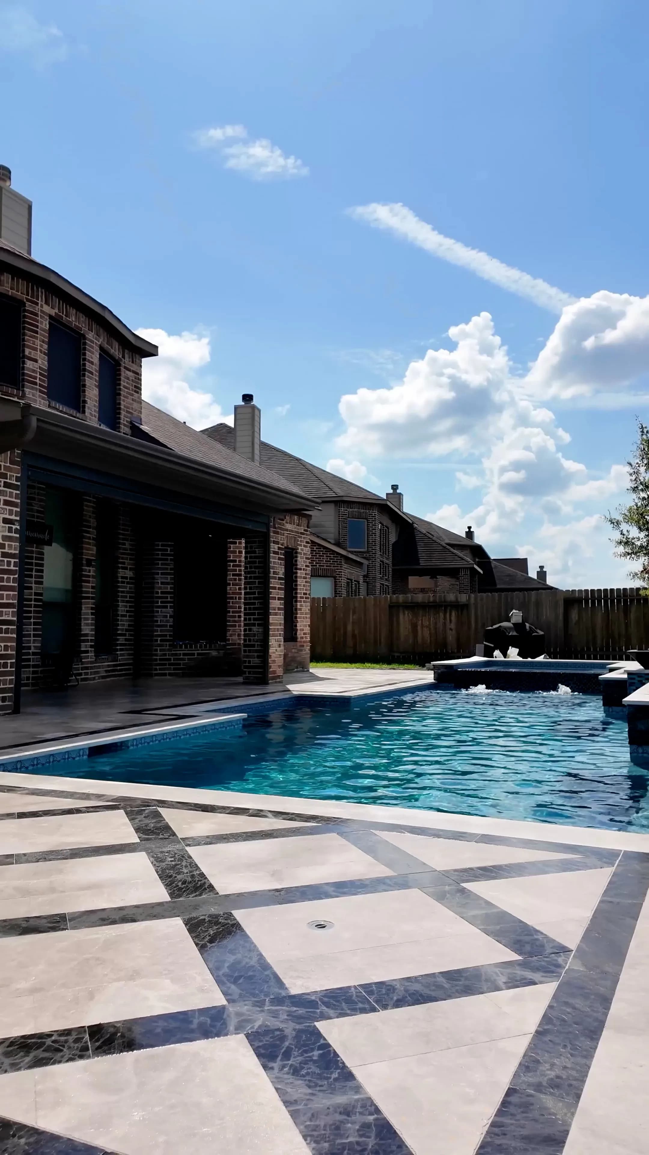 View across the pool to the brick home's covered patio at this Cypress project