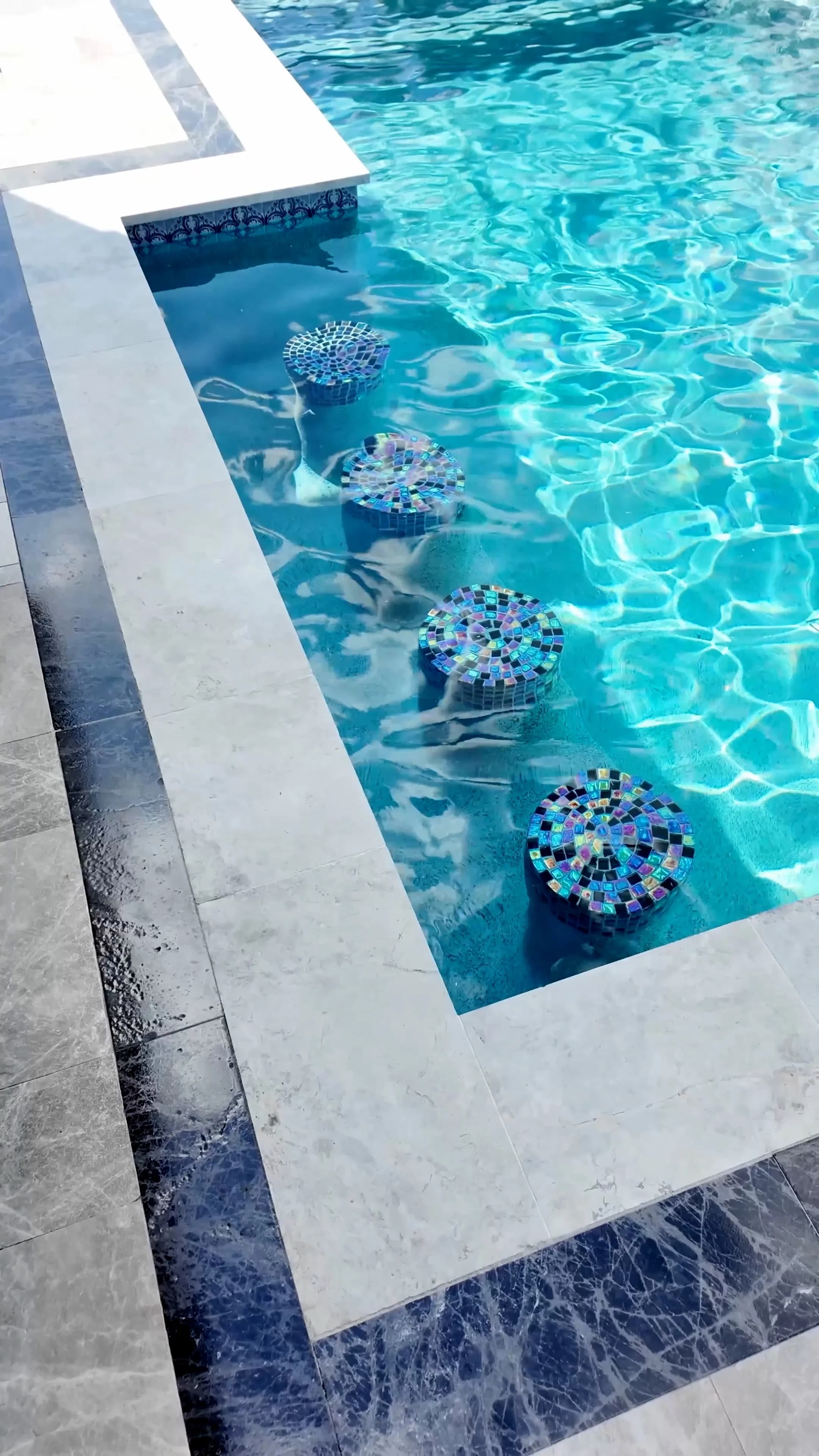 Four iridescent glass-mosaic swim-up stools beneath the water along the pool's edge