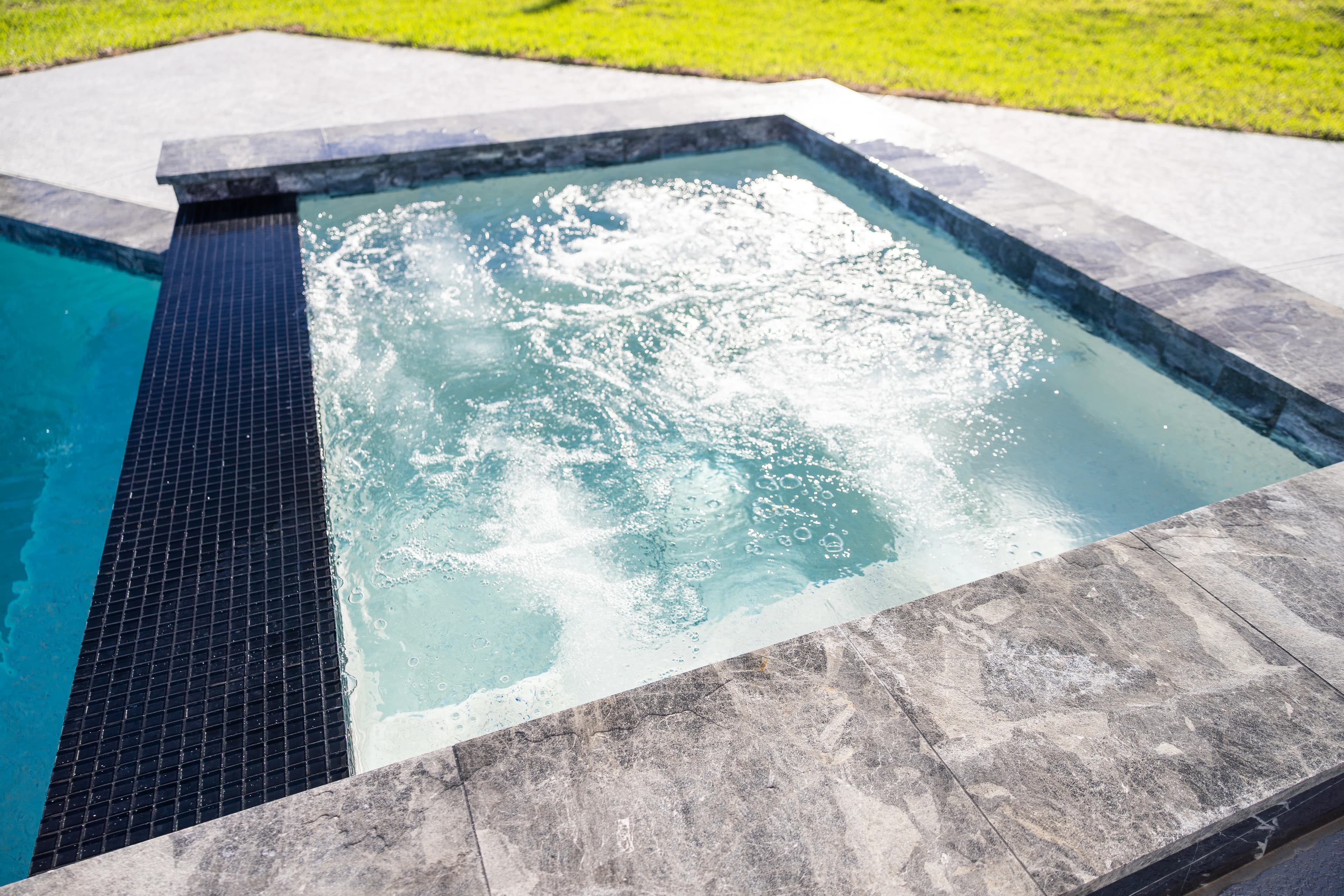 Bubbling spa trimmed in black glass tile and gray marble coping at a Missouri City pool