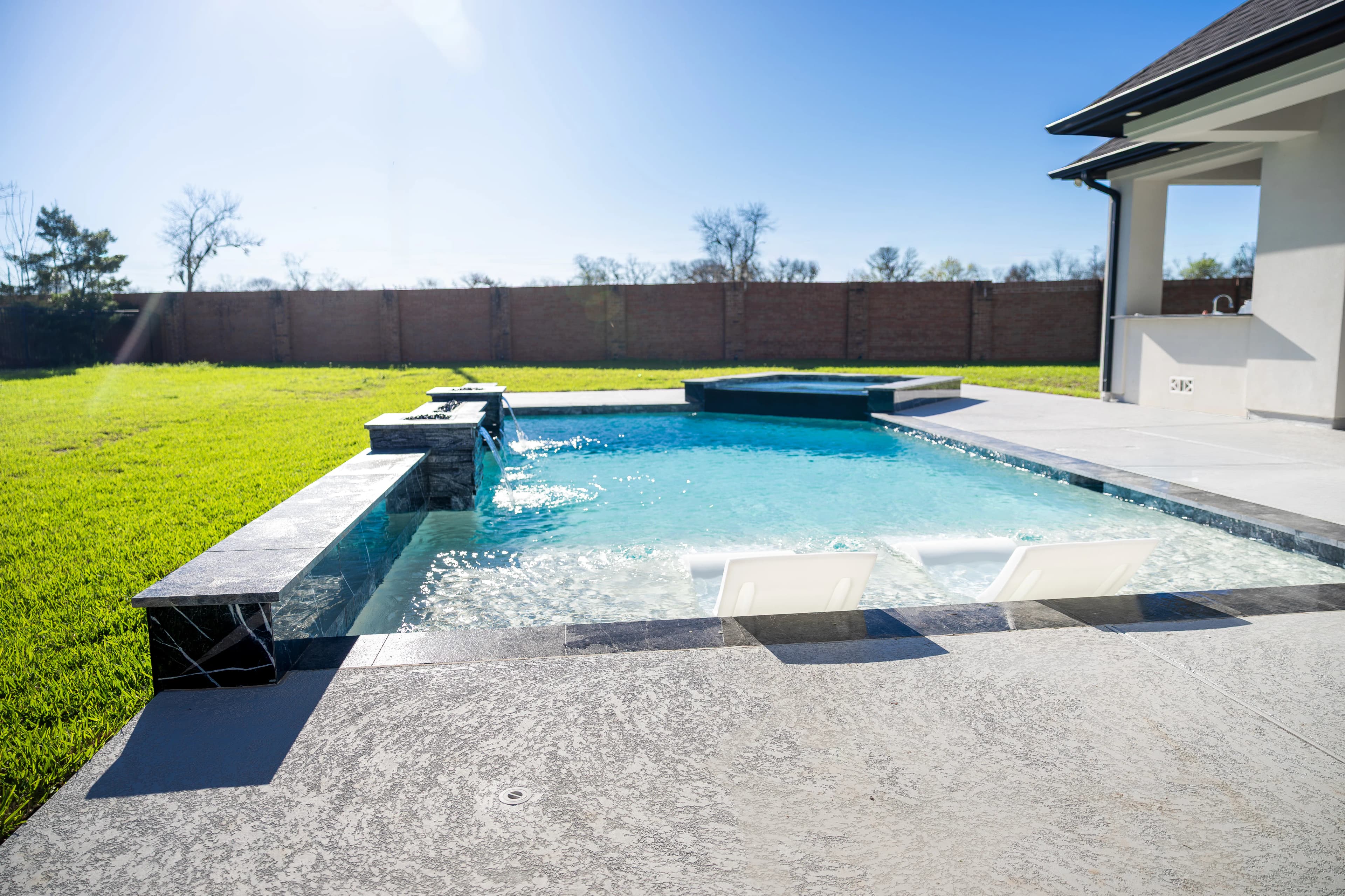 Fire-topped pillars and spillways along the pool's raised wall, covered patio beyond, Missouri City, TX