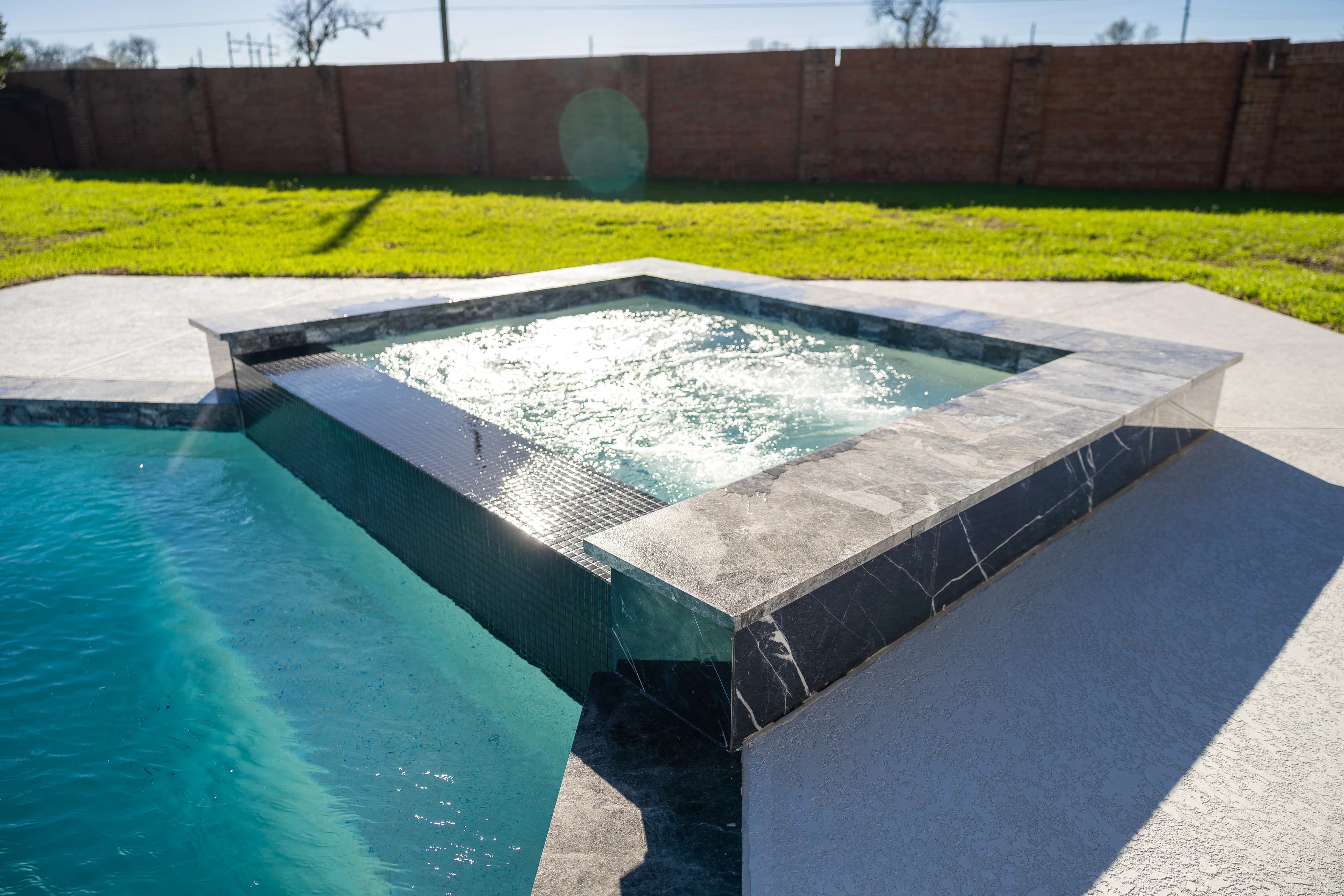 Sunlit spa with glass-tile spillway and marble surround at a Missouri City backyard pool